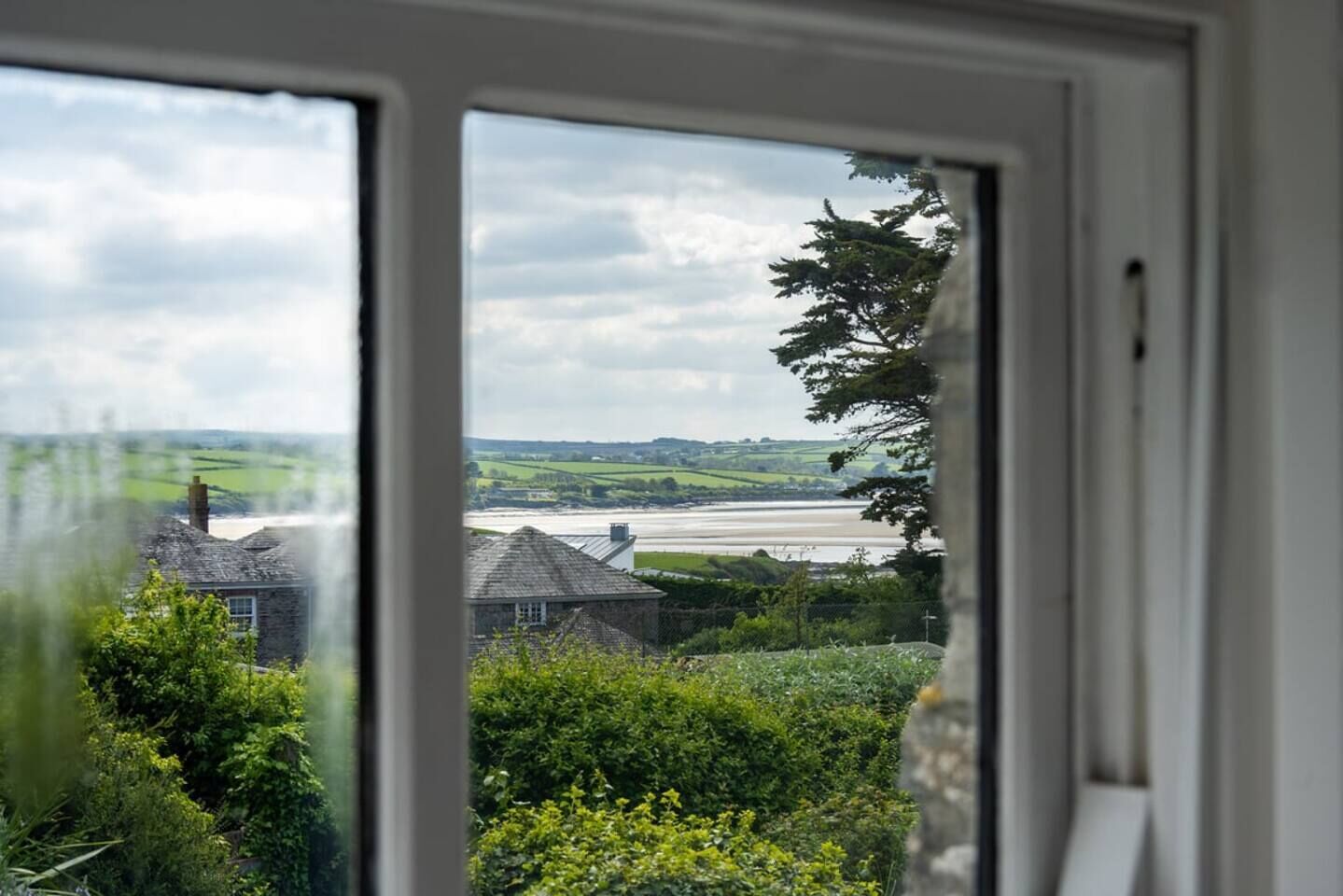 Une vue à travers une fenêtre sur une rivière, de la verdure et un bâtiment en pierre.