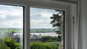 Blick durch ein Fenster auf einen Fluss, Grünflächen und ein Steinhaus.