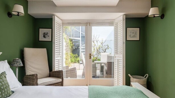 Ein Schlafzimmer mit einem Bett, einem Sessel, einem Fenster mit Fensterläden und Blick nach draußen.