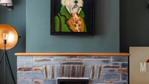 Ein Zimmer mit Kamin aus Stein, einem gerahmten Bild von einem Hund, einer Lampe und einer Vase.