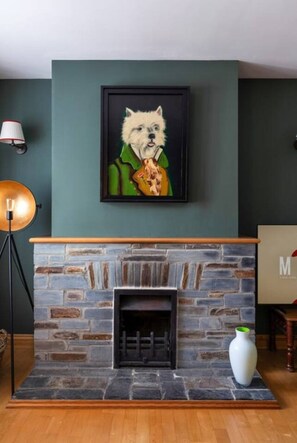 Ein Zimmer mit Kamin aus Stein, einem gerahmten Bild von einem Hund, einer Lampe und einer Vase.