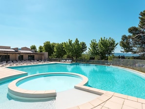 Ein Pool mit gebogener Form, umgeben von Liegestühlen und einem Gebäude mit einem Ziegeldach.