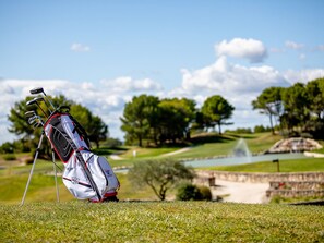 Ein Golfbag mit Schlägern auf einer grünen Wiese, im Hintergrund ein Teich und Bäume.