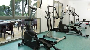 Ein Fitnessraum mit diversen Trainingsgeräten, großen Fenstern und Blick auf eine Außenbestuhlung.
