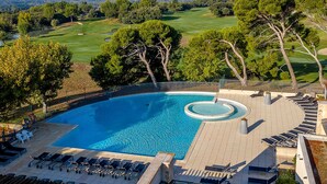 Ein Pool mit einem runden Whirlpool, umgeben von Liegestühlen und einer Sonnenterrasse.