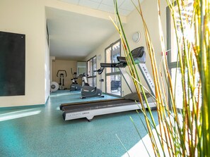 Une salle de sport équipée de tapis de course, de vélos d’exercice et d’un mur recouvert de miroirs.