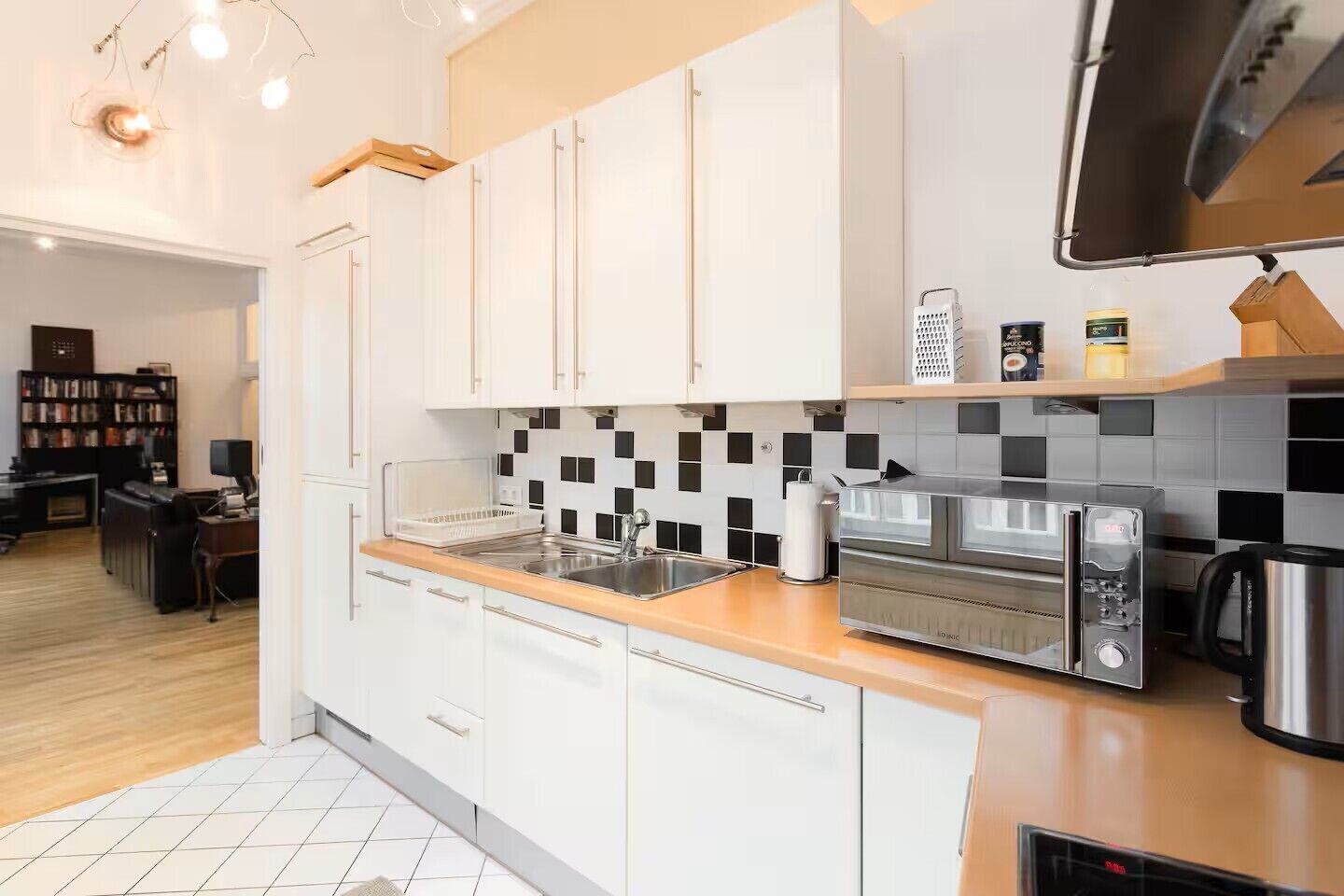 Een moderne keuken met witte kasten, een zwart-wit betegelde spatwand, een ingebouwde oven en een koffieapparaat.