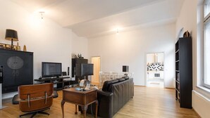 Un salon moderne comprenant un canapé, un fauteuil en bois, une table basse, un téléviseur et une bibliothèque.