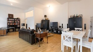 Un salon moderne comprenant un canapé, un téléviseur, une bibliothèque et un coin repas avec des chaises et une table.