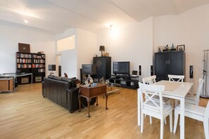 A modern living room with a sofa, TV, bookshelf, and a dining area with chairs and a table. - Digital nomad Loft (Wien)