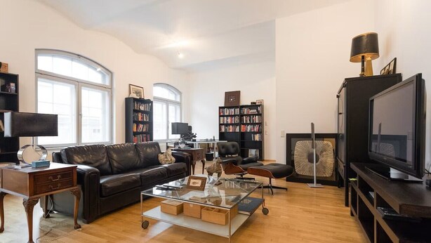 Un salon spacieux avec un canapé en cuir, une table basse, un téléviseur et deux bibliothèques remplies de livres.