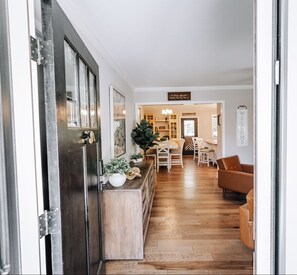 A hallway leading to a dining area with a wooden floor, a bar counter with plants, and a 'WELCOME' sign.