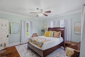 Ein Schlafzimmer mit Bett, Deckenventilator, Schreibtisch, Stuhl, Spiegel und Tür.