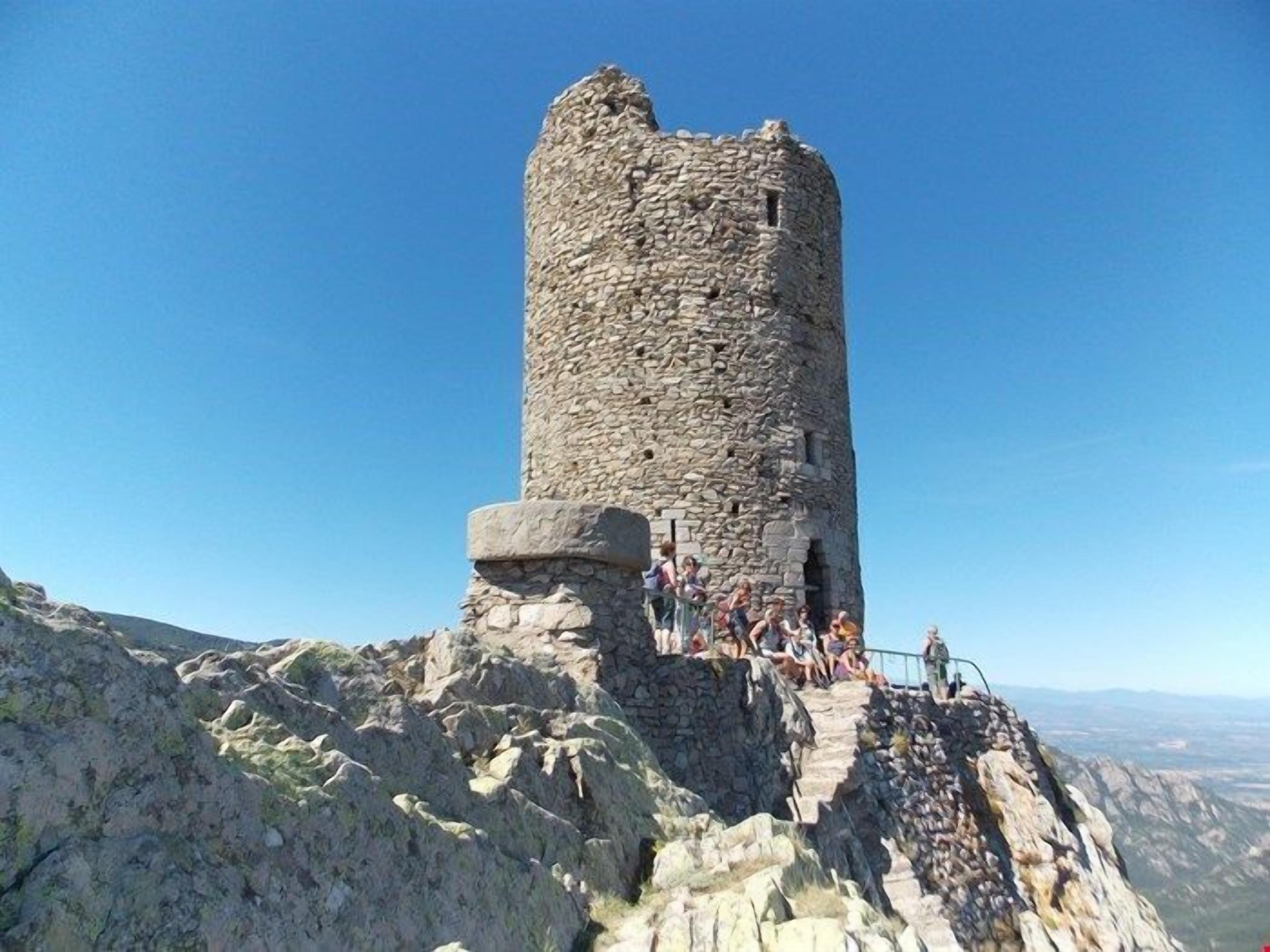 A stone tower with a staircase leading up to it, surrounded by rocky terrain and a clear blue sky.