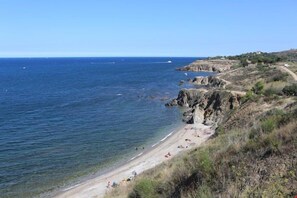 A coastal landscape with a beach, rocky cliffs, and a clear view of the sea.