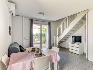 A dining area with a table set for four, a staircase, and a TV in a corner. - Proche de la plage | Accès piscine | AC + balcon (ARGELES-SUR-MER)