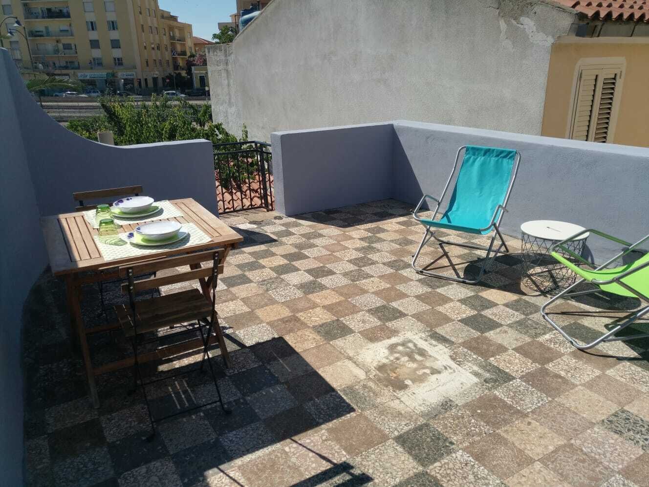 Eine Dachterrasse mit Schachbrettboden, einem Holztisch mit Tellern und zwei Stühlen.
