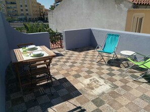 Eine Dachterrasse mit Schachbrettboden, einem Holztisch mit Tellern und zwei Stühlen.