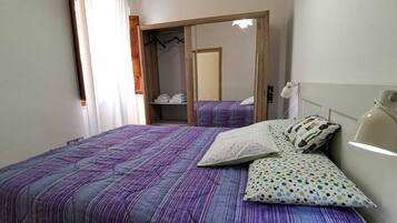 Una camera da letto con un letto, cuscini, un comodino, una lampada e un armadio.