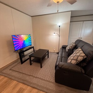 Ein Wohnzimmer mit Flachbildfernseher, Couchtisch, Sofa, Lampe und einer Tür.