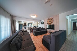 Ein modernes Wohnzimmer mit einer Sofagarnitur, einem Fernseher und einer Küche im Hintergrund.