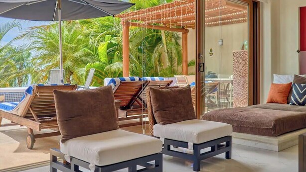 A room with two lounge chairs, a small table, and a view of palm trees. - Beachfront Resort-Style Villa. Pickleball, tennis, Pools, Restaurant (Cruz de Huanacaxtle)
