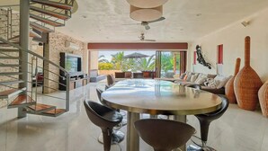 A modern living room with a large round table, black chairs, a TV, and a spiral staircase. - Beachfront Resort-Style Villa. Pickleball, tennis, Pools, Restaurant (Cruz de Huanacaxtle)