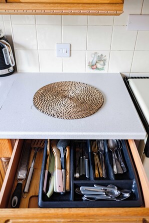 A kitchen with a woven placemat on the counter, a drawer with utensils, and a tiled backsplash.