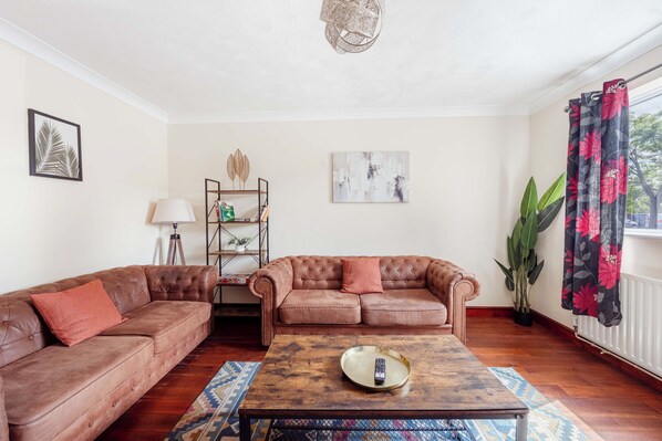 A living room with two brown leather sofas, a wooden coffee table, a lamp, a plant, and artwork on the walls.