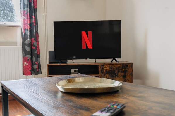 A television with a Netflix logo, a remote control, and a decorative tray on a wooden table.