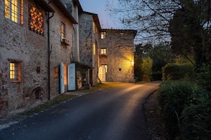 A narrow street flanked by stone buildings with arched doorways and windows, leading to a gated entrance. - Villa delle Silerchie 10, Emma Villas (Camaiore)