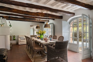 A dining area with a rustic wooden table, wicker chairs, and a view through an arched doorway. - Villa delle Silerchie 10, Emma Villas (Camaiore)