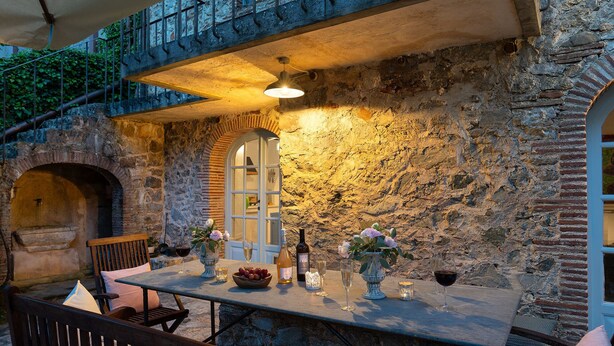 An outdoor dining area with stone walls, a table set with wine glasses, and a rustic ambiance. - Villa delle Silerchie 10, Emma Villas (Camaiore)