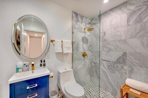 Ein modernes Badezimmer mit einer gläsernen Dusche, einer weißen Toilette, einem blauen Waschtisch und einem runden Spiegel.
