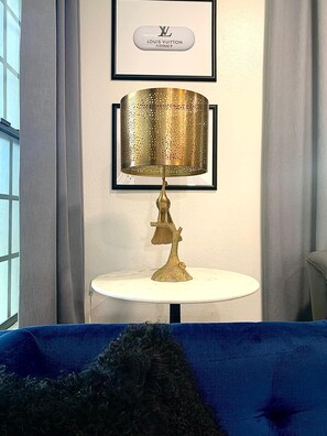 A room with a framed Louis Vuitton sign, a gold lamp on a white table, and a blue sofa. - Stylish 2BR/King Bed, Pool & Spa/Walk to Strip & UNLV (Las Vegas)