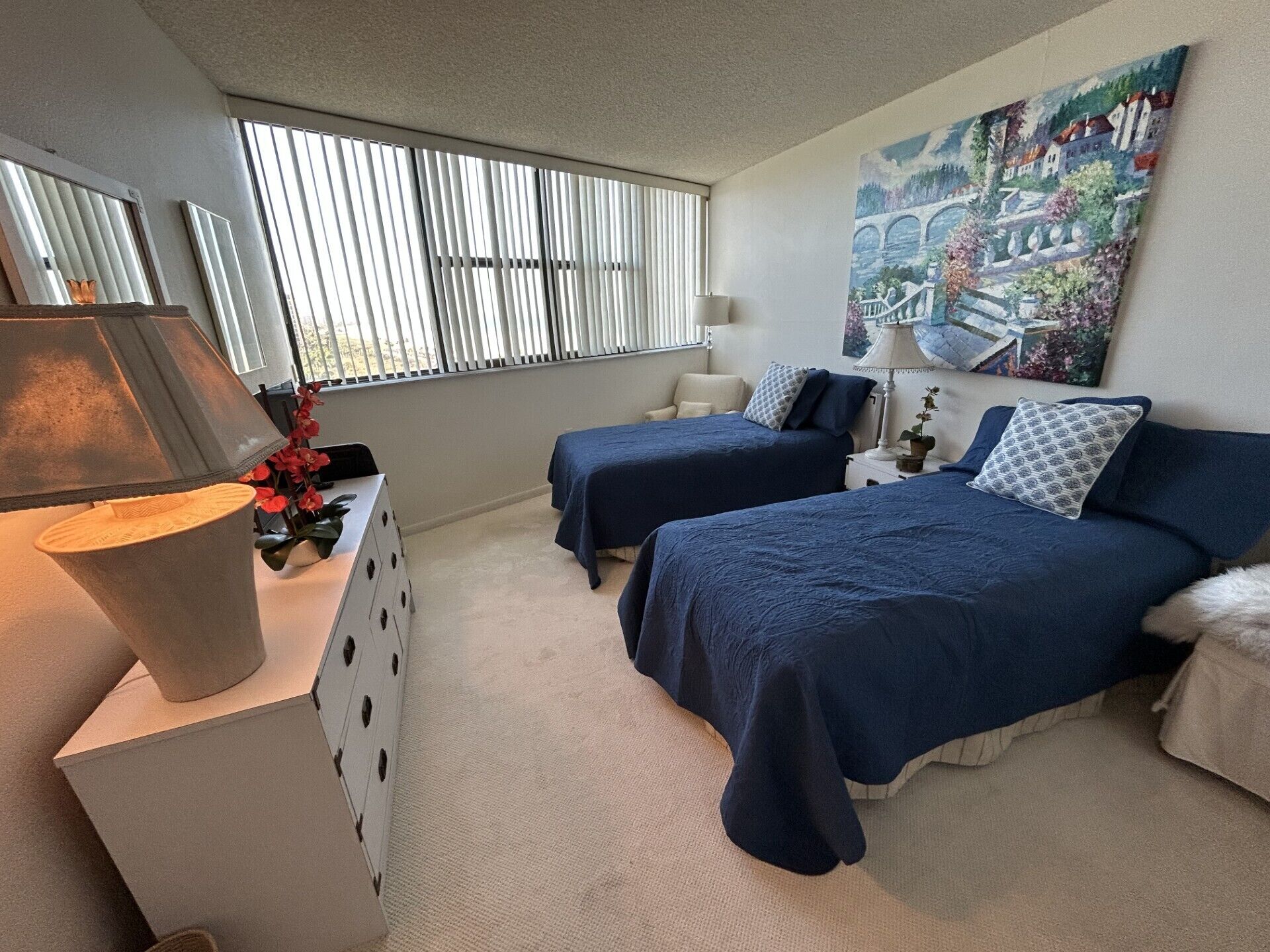 Een slaapkamer met twee bedden, een dressoir, een lamp en een schilderij aan de muur.