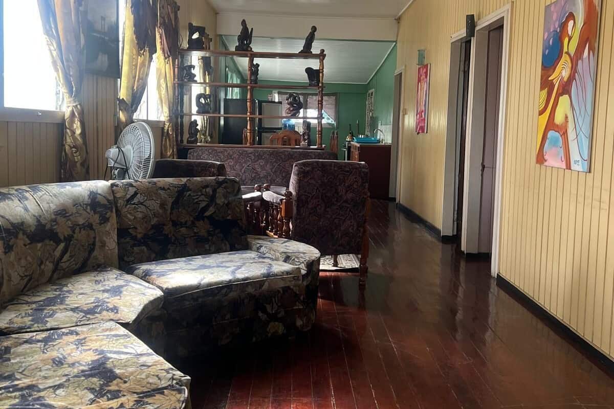 Un pasillo con suelo de madera, un sofá, una silla y un ventilador.