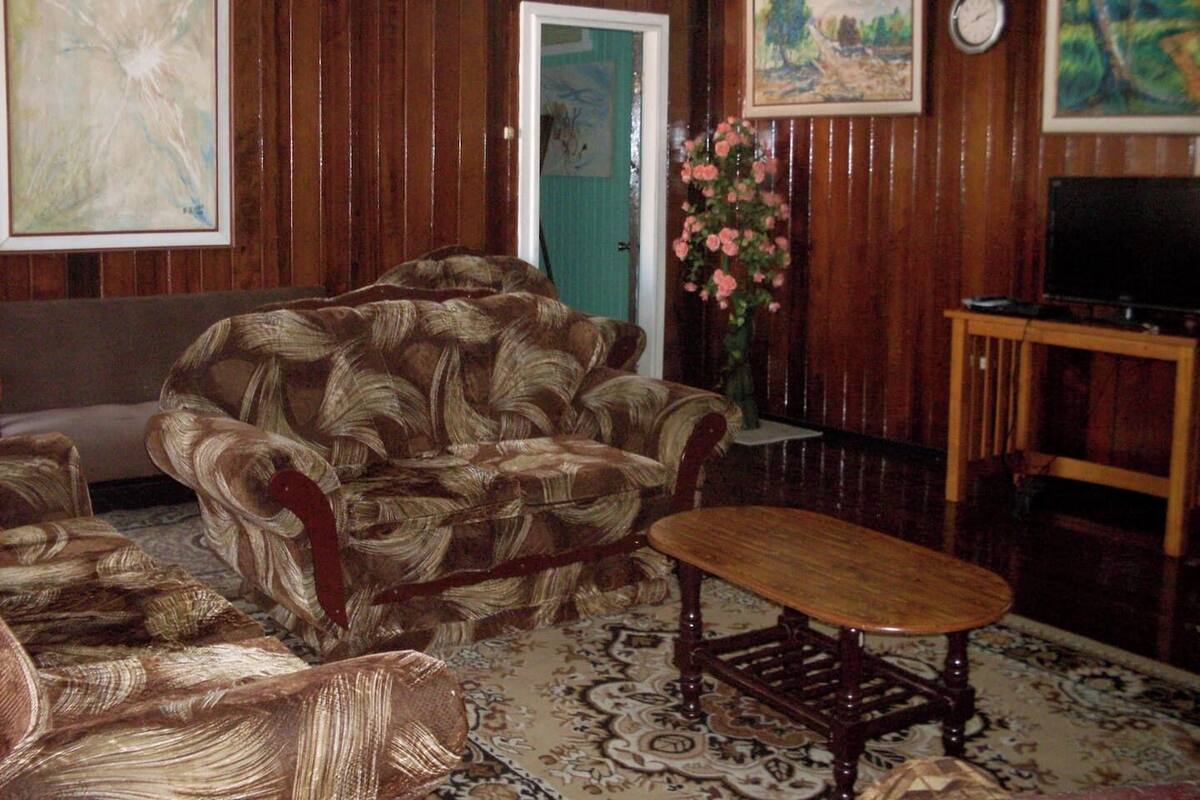 Una habitación con un sofá estampado, una pequeña mesa de madera, un televisor sobre un mueble bajo y una puerta con marco verde.