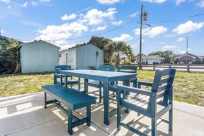 A picnic table with benches, a small shed, and a clear sky. - King's Cottage | Steps from Kure Beach Pier | (Kure Beach)