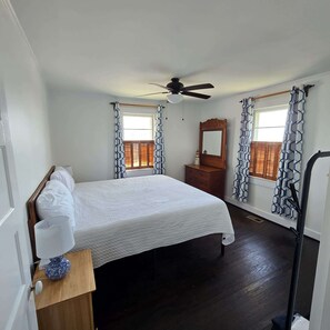 A bedroom with a bed, a dresser, a mirror, and a ceiling fan. - King's Cottage | Steps from Kure Beach Pier | (Kure Beach)
