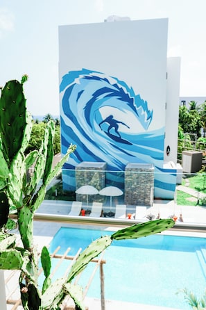 A pool area with a cactus plant, a mural of a surfer, and a stone structure. - Peace Love & Bitcoin - 2BR with Surf Views (El Zonte)