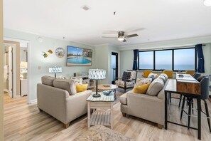 Ein Wohnzimmer mit einer Couch, einem Couchtisch, einem Esstisch mit Stühlen, einem Deckenventilator und einem großen Fenster mit Aussicht.