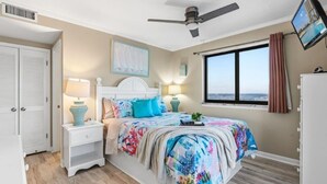 A bedroom with a bed, nightstands, a ceiling fan, a window with curtains, and a TV on the wall. - Myrtle Beach Resort Renaissance Tower #2001 (Myrtle Beach)