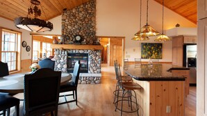 Una cocina amplia con chimenea de piedra, techo de madera y zona de comedor con una mesa redonda y sillas.