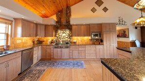 Una cocina amplia con armarios de madera, encimeras de granito, una chimenea de piedra y una isla grande.