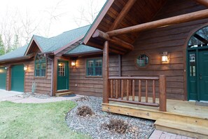 A log cabin with a porch, green doors, and a gravel driveway. - The Sanctuary on the Spirit River Flowage (Tomahawk)