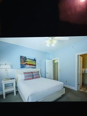 A bedroom with a bed, a nightstand, a painting, and a door leading to another room.