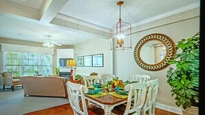 A dining area with a wooden table set for four, surrounded by white chairs. A chandelier hangs above the table, and a large mirror with a decorative frame is on the wall. - Cozy 2-bedroom townhome in superb Williamsburg with AC and gym access (Williamsburg)
