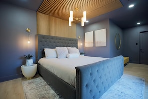 A modern bedroom with a large bed, a wooden slatted ceiling, and a wall-mounted light fixture.