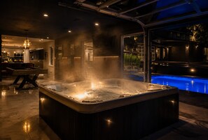 Ein modernes, überdachtes Whirlpool-Becken mit Blick auf einen Außenpool, einen Essbereich und eine Küche.